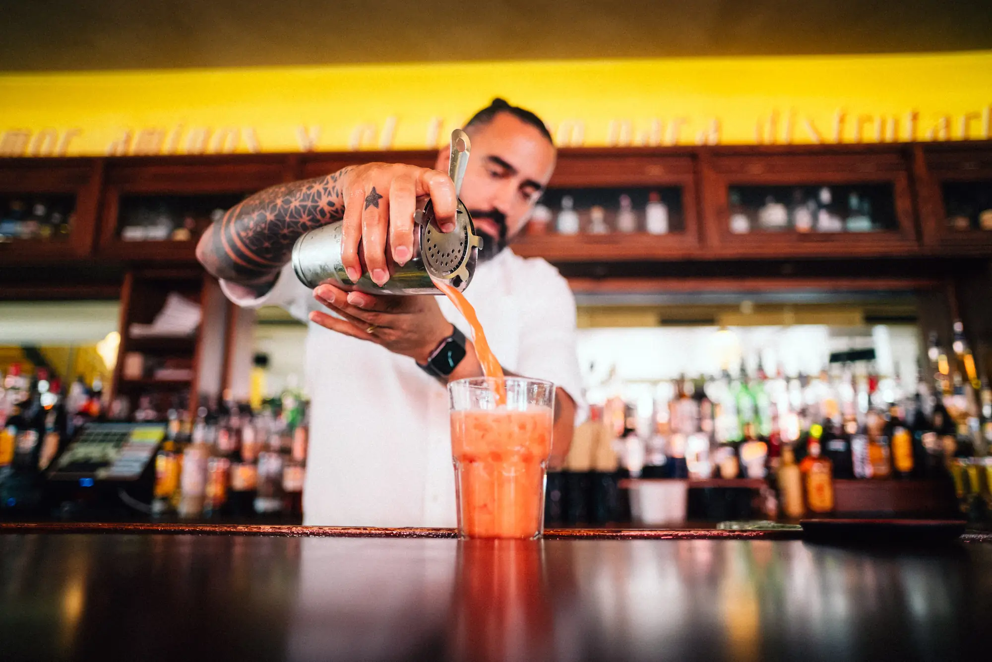Barmann schüttet orangefarbenen Drink aus einem Shaker ins Cocktailglas
